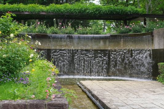 A water fall in a garden with flowers and trees